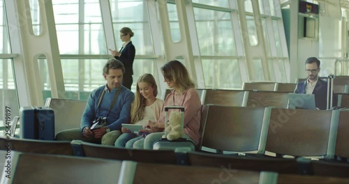 Wallpaper Mural Caucasian family with a daughter sitting in the departure hall at the airport, talking and watching something on the tablet computer. Torontodigital.ca