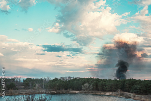 Forest fire near the lake and stunning sky with light and dark clouds background.