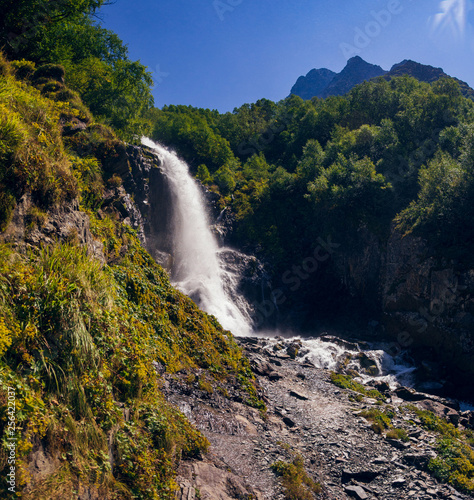 A high mountain waterfall makes its way through huge stones on a clear  summer day. High in the Caucasian mountains  in the outskirts of Dombai.chuhursky waterfall