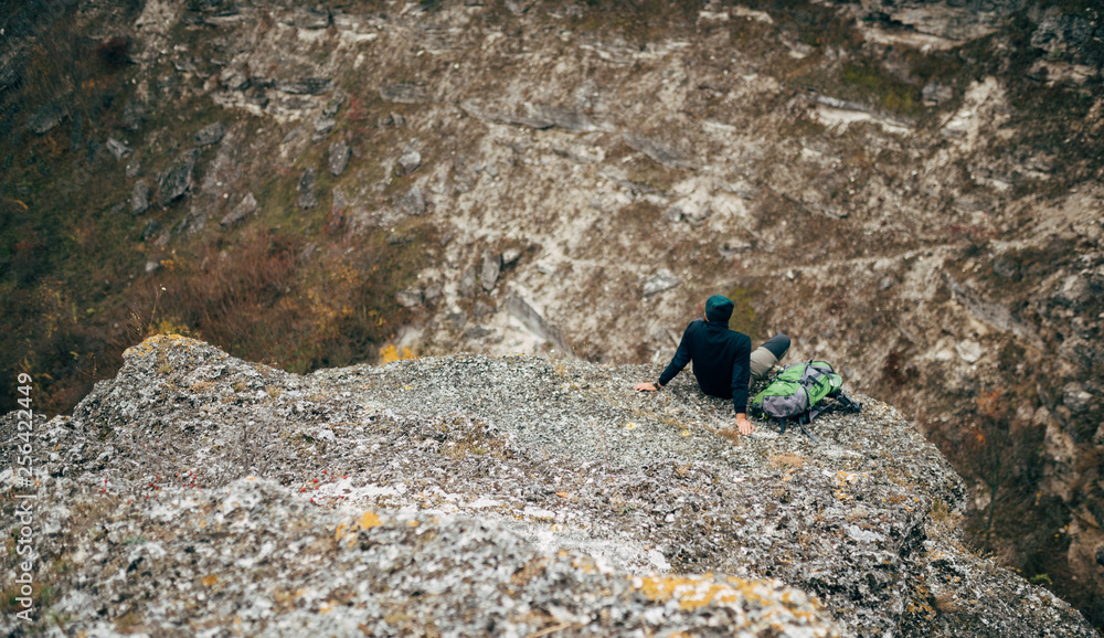 Landscape overhead rear view of hiker man relaxing in mountains after hiking. Outdoors shot of traveler male sitting alone on rock, have a break after mountaineering. Travel and lifestyle concept