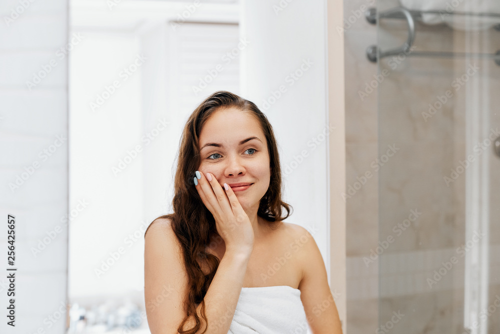 Woman touching wet hair and smiling while looking in the mirror. Portrait of girl in bathroom applying conditioner and oil.Portrait of female uses protection moisturizing cream. Woman touching wet hair and smiling while looking in the mirror. Portrait of girl in bathroom applying conditioner and oil.Portrait of female uses protection moisturizing cream.