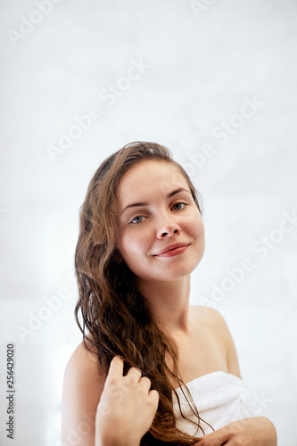 Hair and body care. Girl uses protection moisturizing cream and oil. Beautiful young woman touching her wet hair with hands and smiling while standing in front of the mirror  in bathroom.