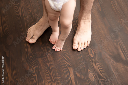 The child makes the first step. Large male legs with small baby legs. Dad helps the child take the first steps. photo