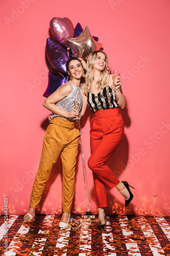 Photography Photo of two happy women 20s in stylish outfit holding festive balloons and drin