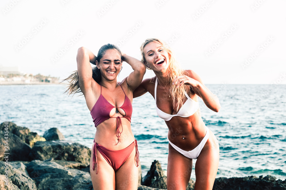 Girls with fitness abs abdominal have fun and laugh a lot together in friendshop at the beach in summer vacation - babes with bikinis enjoying the sun and the ocean - blonde and brunette couple