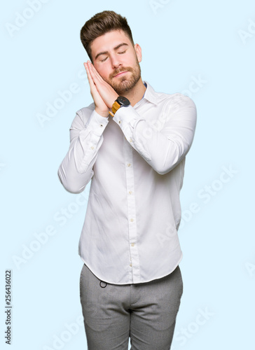 Young handsome business man sleeping tired dreaming and posing with hands together while smiling with closed eyes.