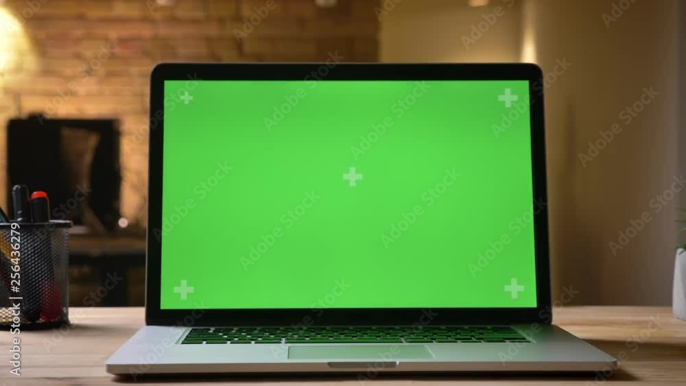 Closeup shoot of the laptop with green screen on the desk in the office indoors with businessman on the blurred background Closeup shoot of the laptop with green screen on the desk in the office indoors with businessman on the blurred background