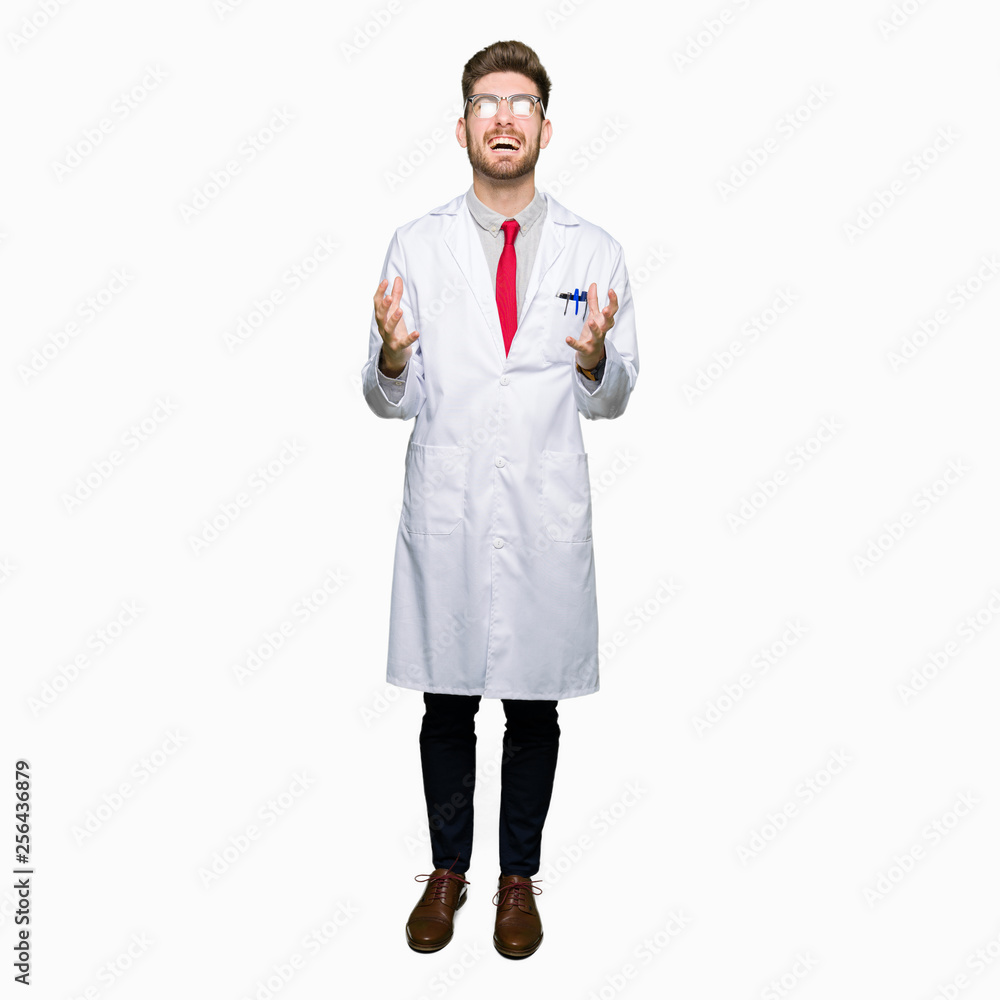 Young handsome scientist man wearing glasses crazy and mad shouting and yelling with aggressive expression and arms raised. Frustration concept.