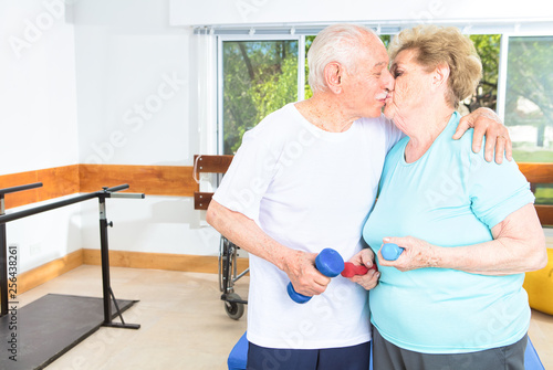 Elderly couple kissing at the gym with weights in their hands. Happiness, fitness and family concept