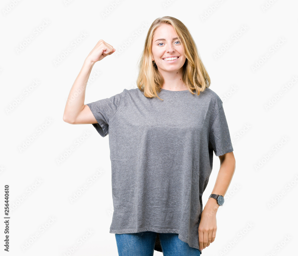 Fototapeta premium Beautiful young woman wearing oversize casual t-shirt over isolated background Strong person showing arm muscle, confident and proud of power