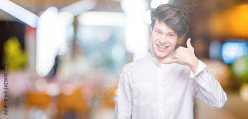 Young handsome business man over isolated background smiling doing phone gesture with hand and fingers like talking on the telephone. Communicating concepts.