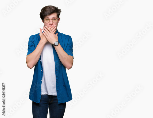 Young handsome man wearing glasses over isolated background shocked covering mouth with hands for mistake. Secret concept.