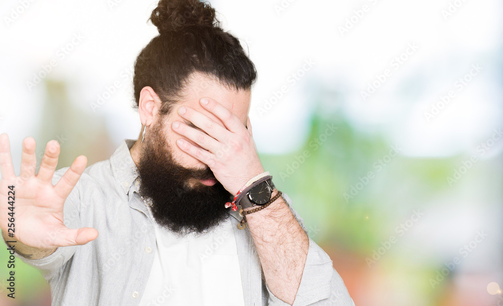 Young man with long hair, beard and earrings covering eyes with hands and doing stop gesture with sad and fear expression. Embarrassed and negative concept. Young man with long hair, beard and earrings covering eyes with hands and doing stop gesture with sad and fear expression. Embarrassed and negative concept.