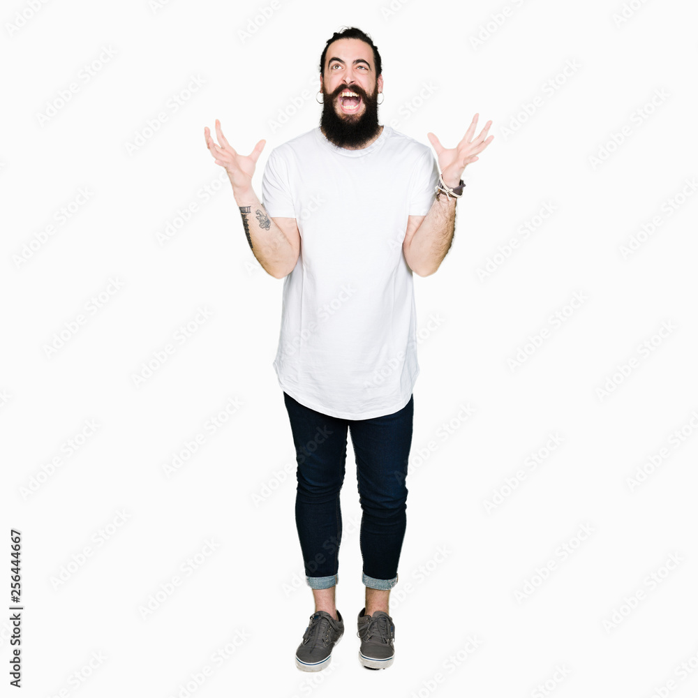 Young hipster man with long hair and beard wearing casual white t-shirt crazy and mad shouting and yelling with aggressive expression and arms raised. Frustration concept. Young hipster man with long hair and beard wearing casual white t-shirt crazy and mad shouting and yelling with aggressive expression and arms raised. Frustration concept.