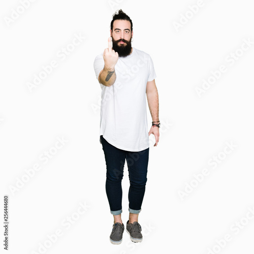 Young hipster man with long hair and beard wearing casual white t-shirt Showing middle finger, impolite and rude fuck off expression
