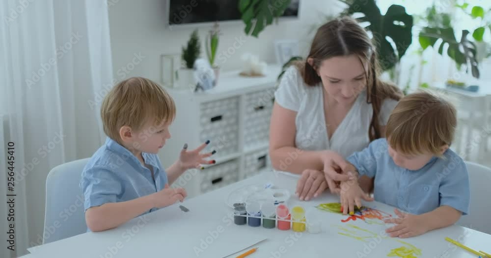 The family has fun painting on paper with their fingers in paint. Mom and two children paint with fingers on paper The family has fun painting on paper with their fingers in paint. Mom and two children paint with fingers on paper