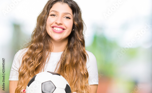 Young adult woman holding soccer football ball with a happy face standing and smiling with a confident smile showing teeth © Krakenimages.com