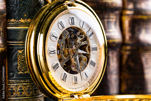 Antique clock on the background of vintage books. Mechanical clockwork on a chain.