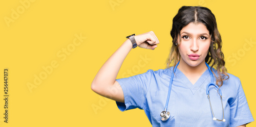 Young adult doctor woman wearing medical uniform Strong person showing arm muscle, confident and proud of power