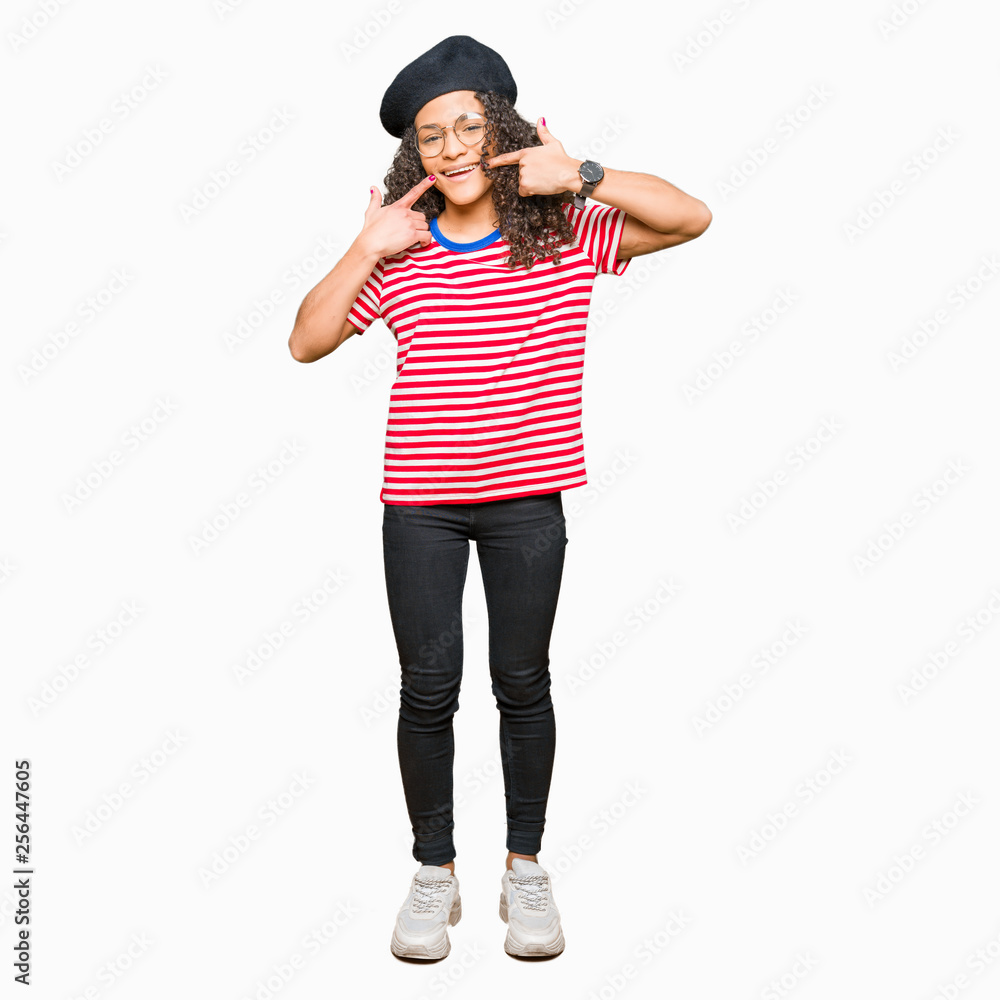 Young beautiful woman with curly hair wearing glasses and fashion beret smiling confident showing and pointing with fingers teeth and mouth. Health concept. Young beautiful woman with curly hair wearing glasses and fashion beret smiling confident showing and pointing with fingers teeth and mouth. Health concept.