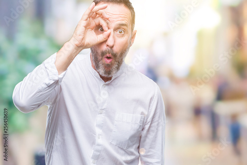 Middle age hoary senior man over isolated background doing ok gesture shocked with surprised face, eye looking through fingers. Unbelieving expression.
