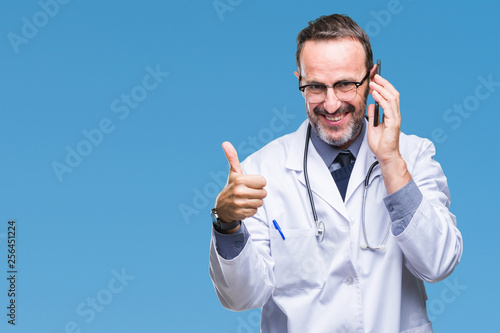 Middle age senior hoary doctor man talking on smartphone over isolated background happy with big smile doing ok sign, thumb up with fingers, excellent sign