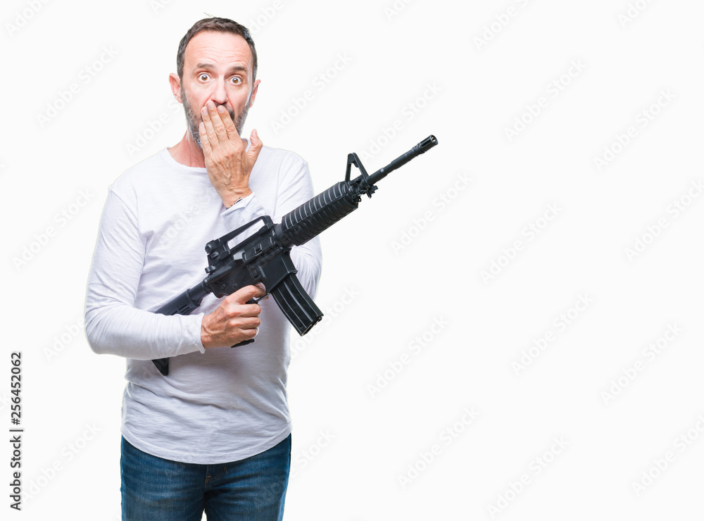 Middle age senior hoary criminal man holding gun weapon over isolated background cover mouth with hand shocked with shame for mistake, expression of fear, scared in silence, secret concept