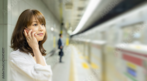 Young Asian woman in the subway station talking on the phone waiting for a train