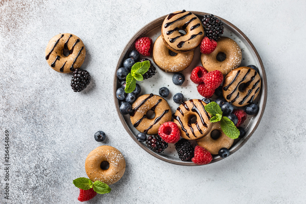 Homemade cinnamon and chocolate mini donuts on the plate with berries and mint on the light grey backgorund