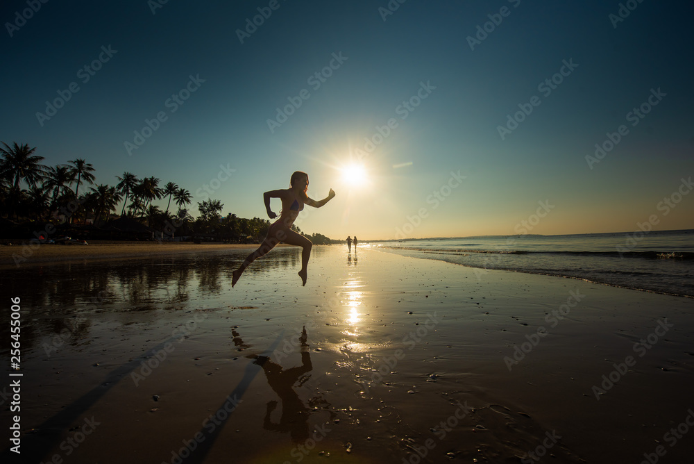 Woman runs barefoot on the beach at sunset. Silhouette of a woman by the sea at sunrise