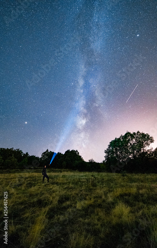 Astrofotografia con una persona iluminando hacia el infinito entre arboles y montañas