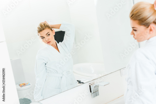 selective focus of woman in white bathrobe playing with hair in bathroom