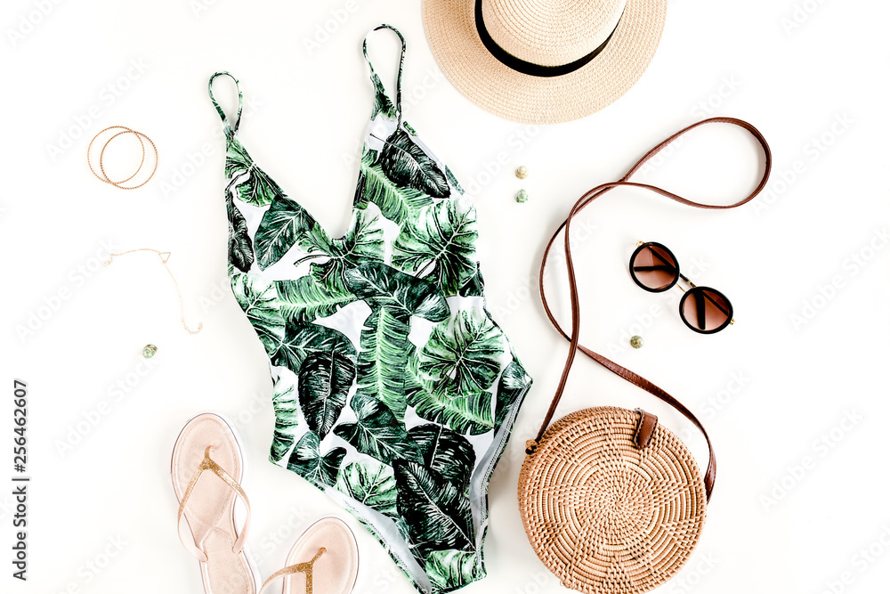 Woman's beach accessories: swimsuit with tropical print, rattan bag, straw hat on white background. Summer background. Flat lay, top view. - obrazy, fototapety, plakaty 