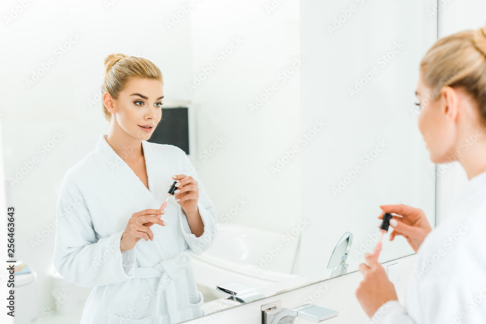 selective focus of beautiful woman in white bathrobe holding lip gloss in bathroom selective focus of beautiful woman in white bathrobe holding lip gloss in bathroom