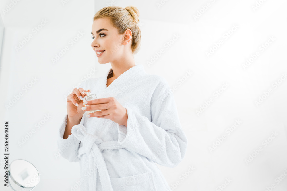 beautiful and smiling woman in bathrobe holding perfume in bathroom beautiful and smiling woman in bathrobe holding perfume in bathroom