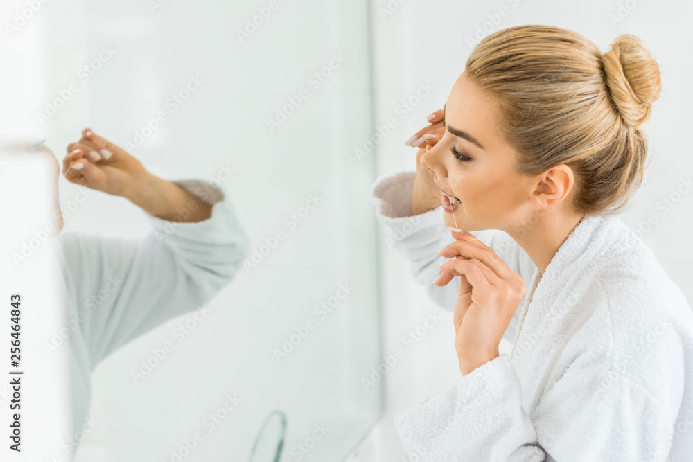 selective focus of attractive and blonde woman in white bathrobe brushing teeth with dental floss selective focus of attractive and blonde woman in white bathrobe brushing teeth with dental floss