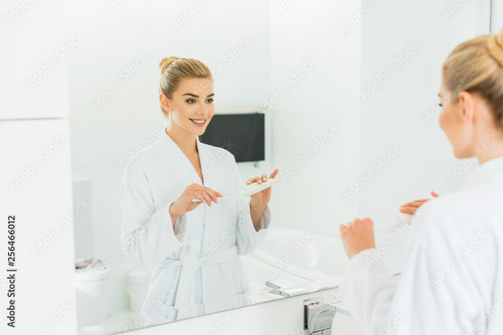 selective focus of smiling woman in bathrobe applying toothpaste on toothbrush in bathroom selective focus of smiling woman in bathrobe applying toothpaste on toothbrush in bathroom