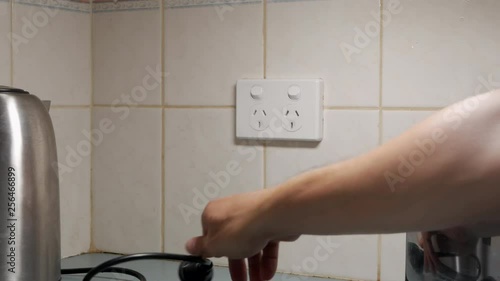 Man turns off power outlet and unplugs the kettle and toaster form the wall socket. LOCKD DOWN SHOT. photo