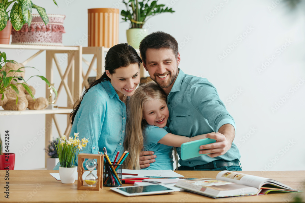 Father, mother and their daughter are smiling while spending time together. A day with family. Young happy couple with child are making a selfie with the smartphone. Education, studying and knowledge Father, mother and their daughter are smiling while spending time together. A day with family. Young happy couple with child are making a selfie with the smartphone. Education, studying and knowledge