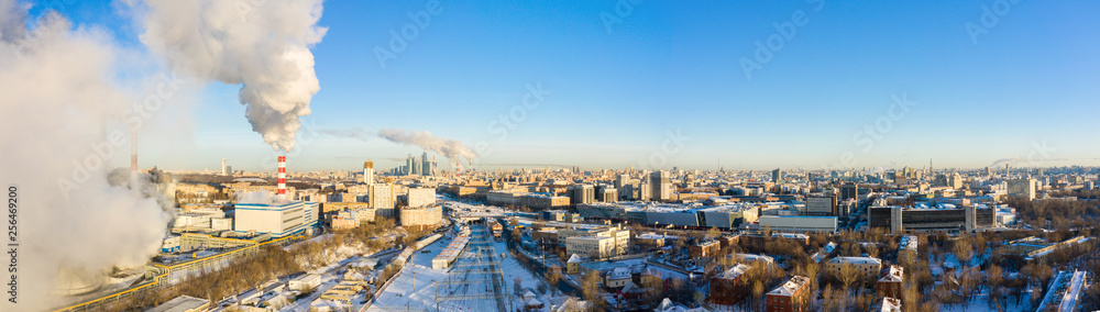 power plant pipes and cooling towers on the background of the panorama of the winter city against blue sky.