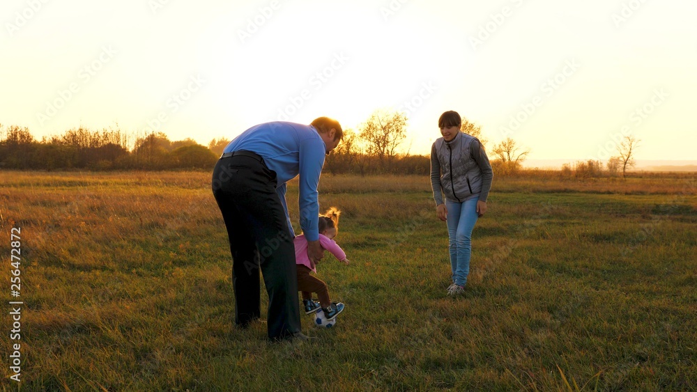 Family playing with younger baby with soccer ball in park at sunset. Happy dad and child kick ball. happy family concept. Slow motion