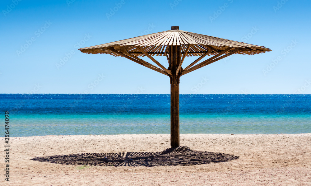 one wooden beach umbrella on the sand on the beach against the blue water of the Red Sea in Egypt Dahab South Sinai