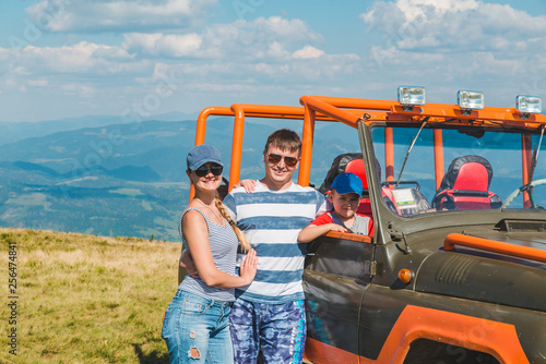 young family posing near suv car with beautiful view of mountains