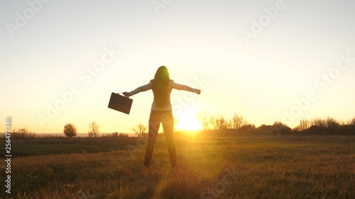 Free business woman with briefcase in her hand and in business suit is success at sunset in bright rays of sun.
