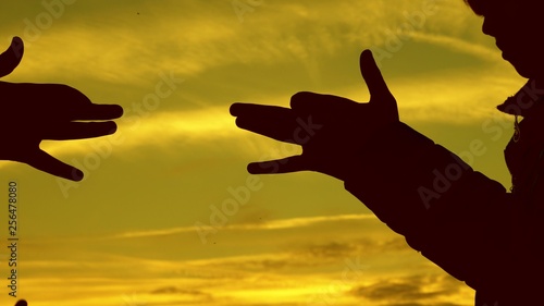 Children make shape of dog shape with hands at sunset. girls hold the gesture of a dog symbol with their fingers against sky. children show with hands the silhouette of an animal. shadow play