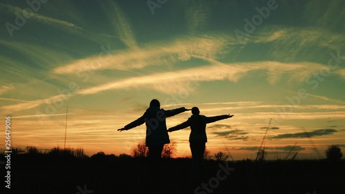 Children play in the evening at sunset. girls superheroes run across the meadow against backdrop of beautiful sky. children dream of flying. concept of happy childhood. teamwork girlfriend