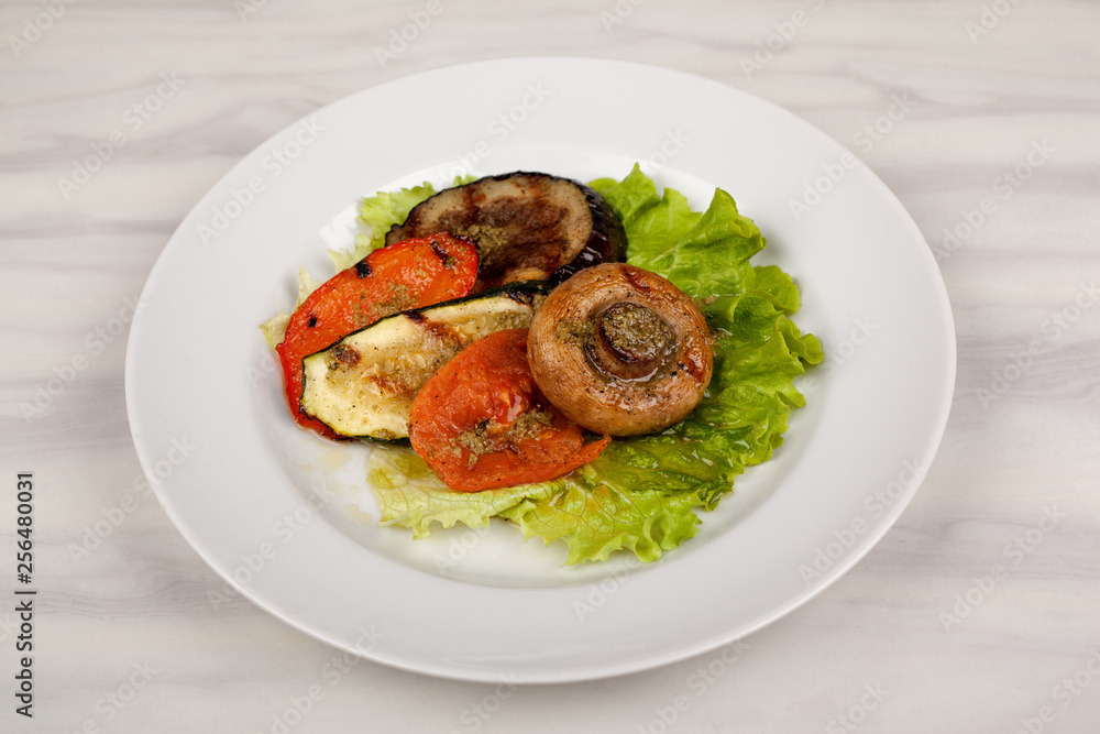 Fried mushroom champignon, eggplant, tomato and green leaf lettuce on a white round plate. Fried mushroom champignon, eggplant, tomato and green leaf lettuce on a white round plate.
