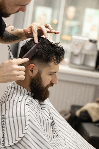 Handsome bearded man, having hair cut by scissors at barber shop .