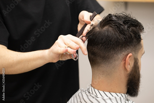 Handsome bearded man, having hair cut by scissors at barber shop .