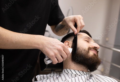 Client during beard shaving in barber shop 